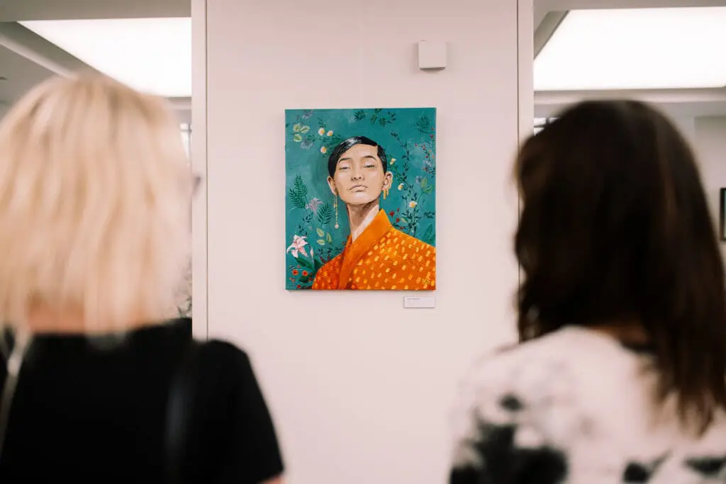 two women looking at a painting on a wall in a gallery