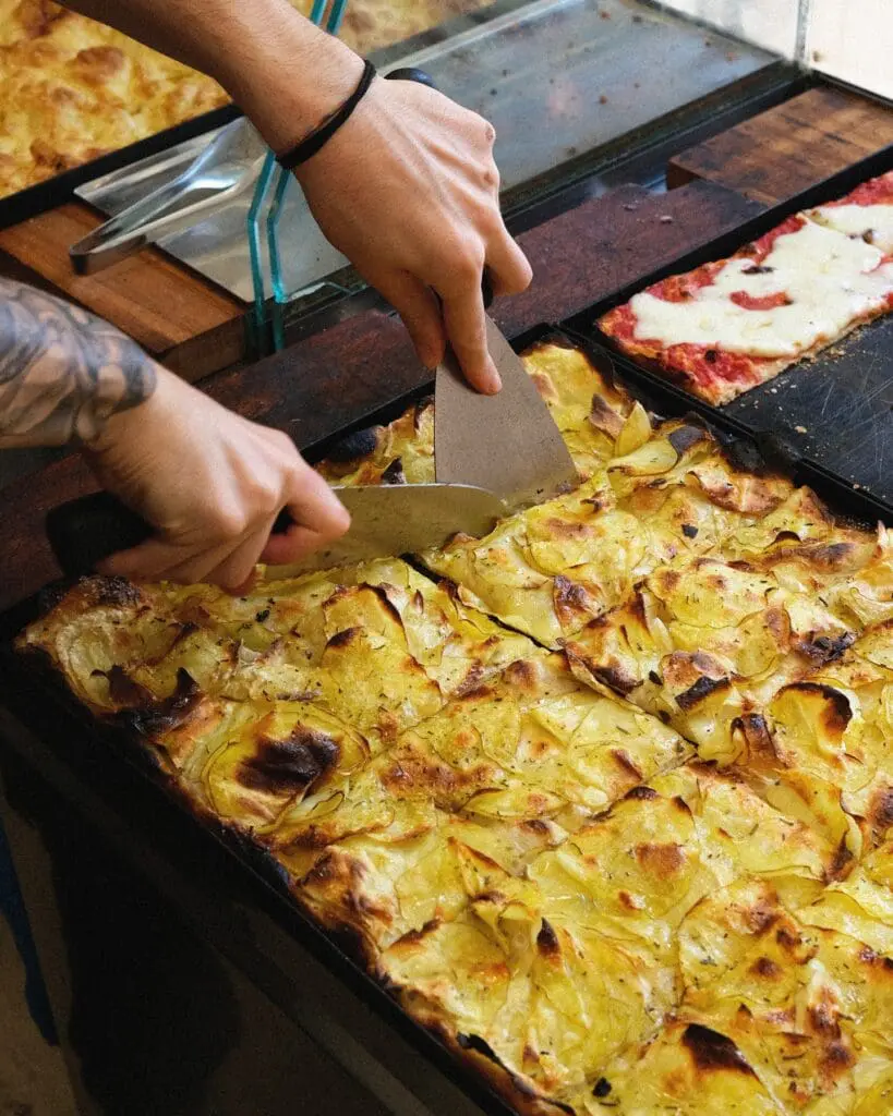 Slicing and serving Pizza con Patate in Pantera in Rome.