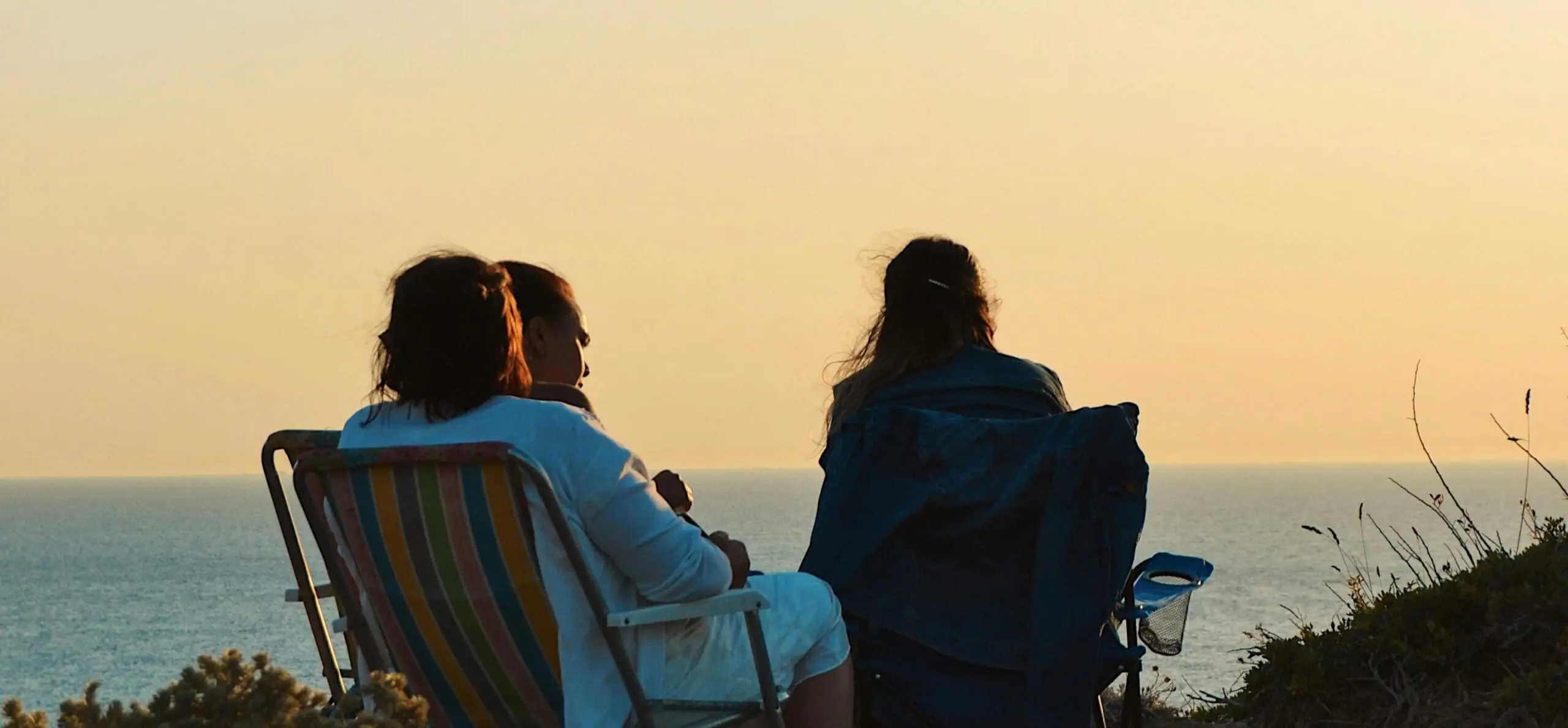 Three people from Athene Club sat down on camping chairs looking out onto the ocean