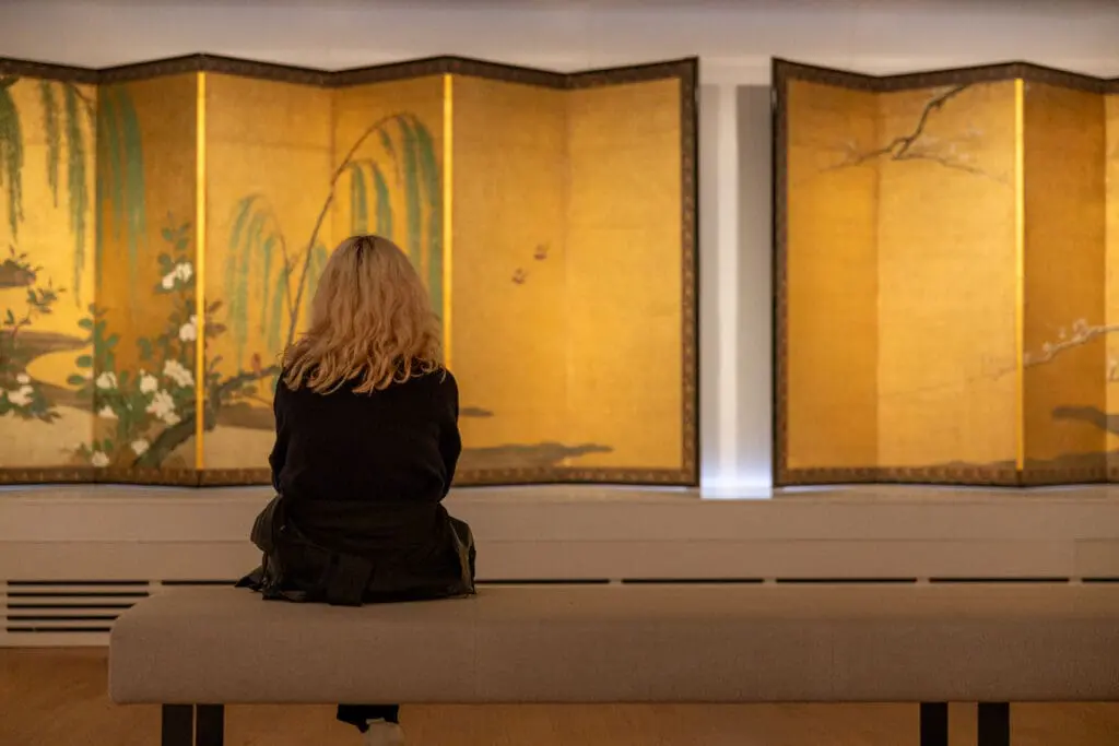 person with blonde hair sitting in front of artwork at the Rijksmuseum in Amsterdam