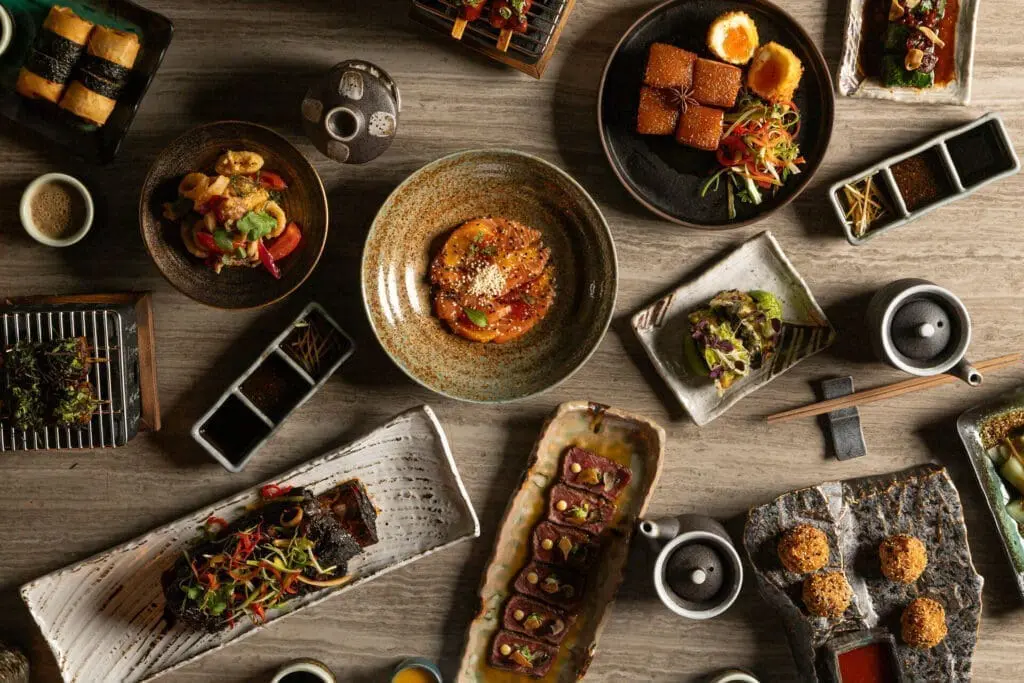 Assorted gourmet Asian dishes on a wooden table at art'otel Yezi restaurant Rome, featuring vibrant colors and artistic presentation.