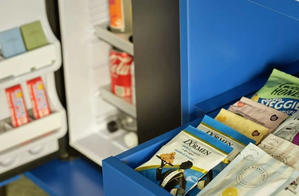 In‑room minibar at art'otel Hotel next to Battersea Power Station featuring curated snacks, soft drinks and modern blue drawer storage design.