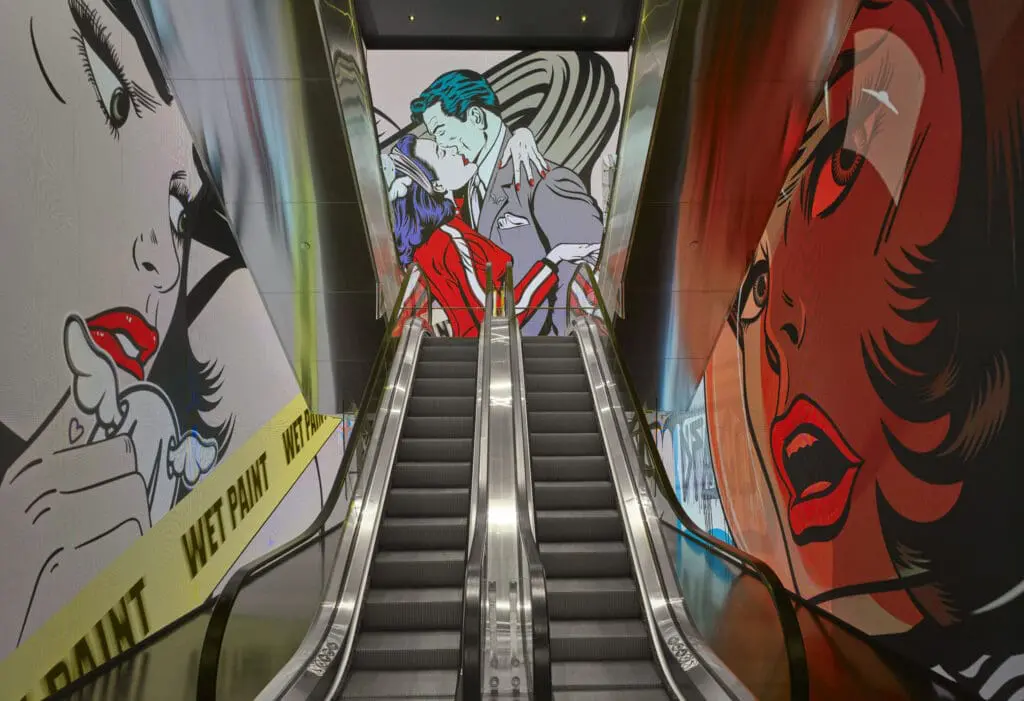 Escalator surrounded by vibrant pop art murals featuring comic-style characters at art'otel London Hoxton Old Street hotel with spa.
