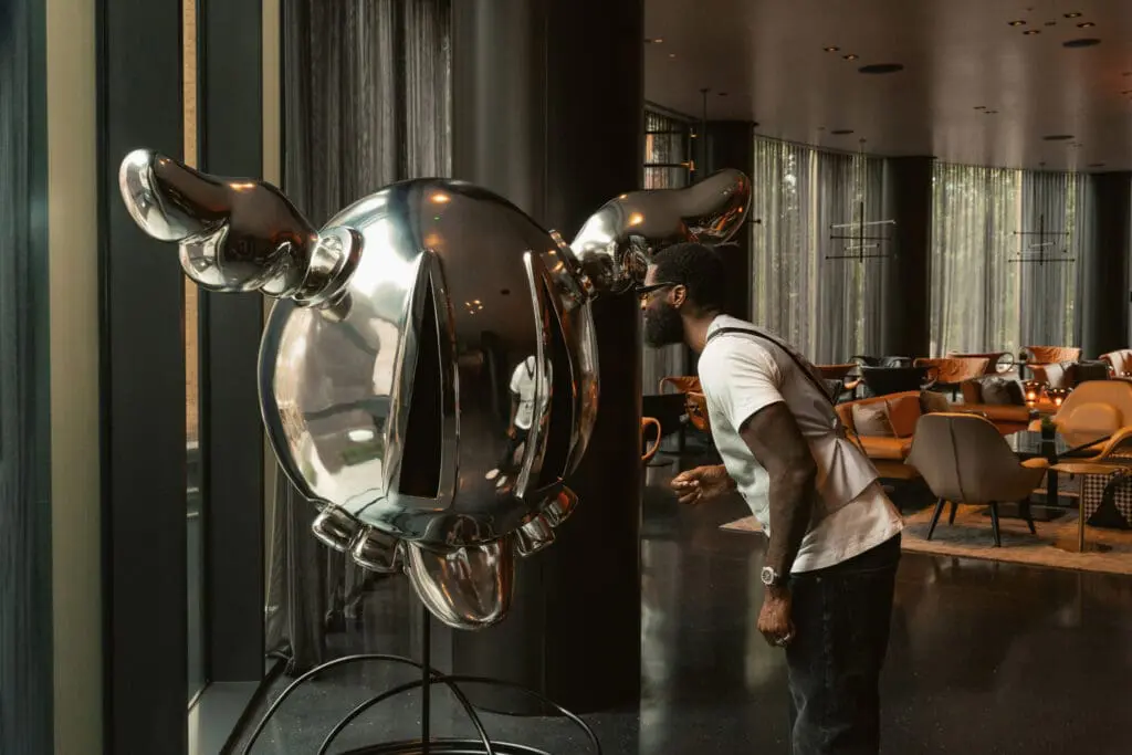Person observing a shiny metallic sculpture with wing-like details inside art'otel London Hoxton Old Street hotel with pool.