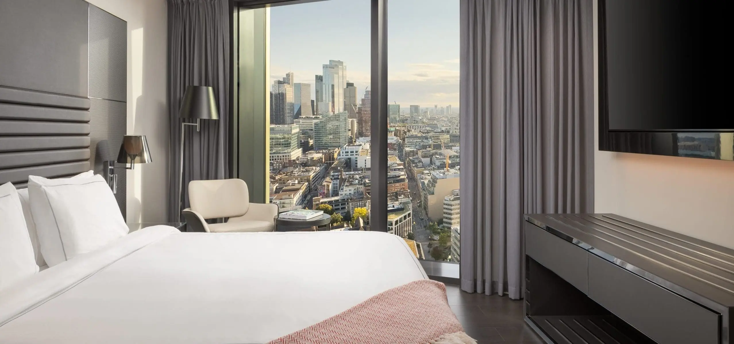 Modern hotel room with large bed and city skyline view at art'otel London Hoxton