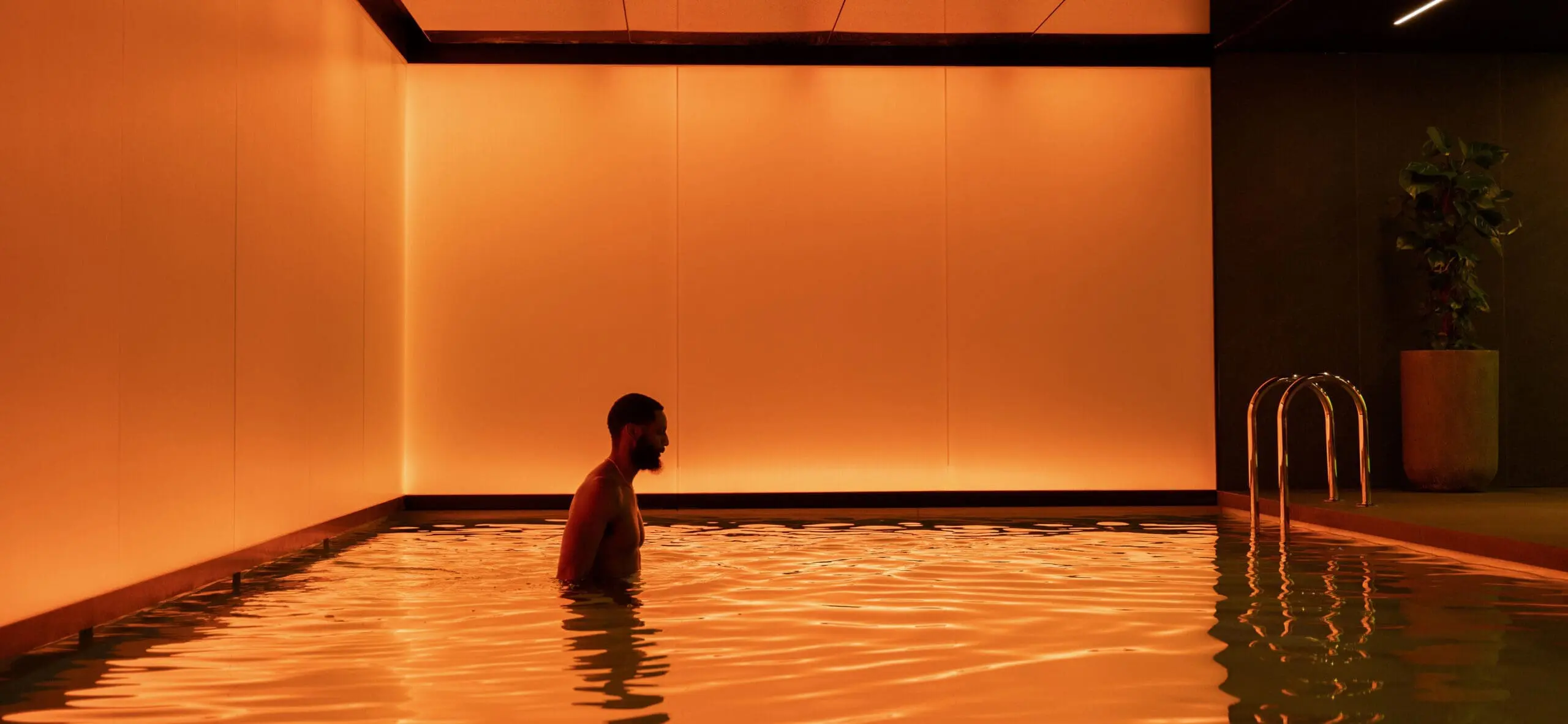 Person standing in an indoor swimming pool with warm orange ambient lighting and modern minimalist design at art'otel London Hoxton Shoreditch hotel with pool.