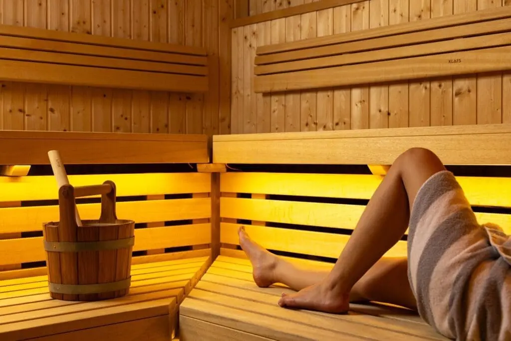 Indoor swimming pool at art'otel London Hoxton Old Street hotel with pool, featuring sleek gray loungers, folded towels, and soft purple ambient lighting.