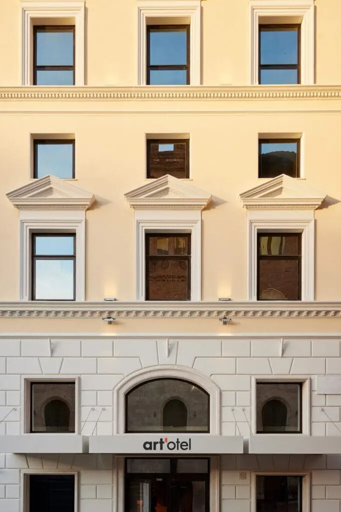 Detailed exterior facade of art’otel Rome art hotel featuring classic architectural windows with ornate pediments and beige walls.