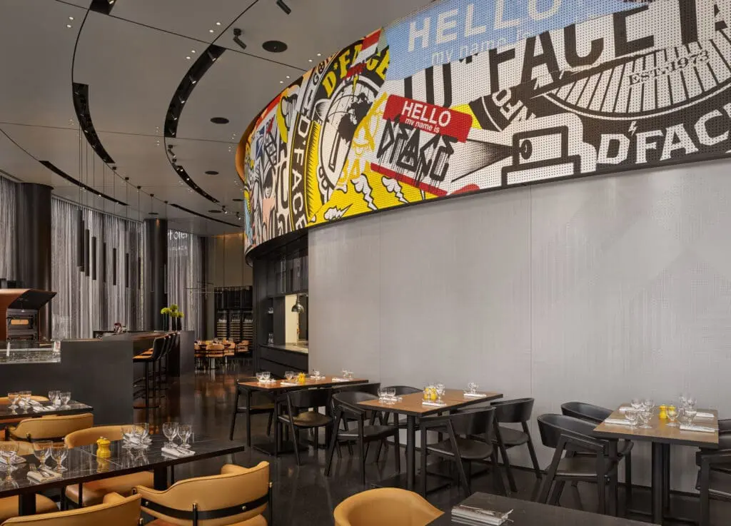 Contemporary restaurant interior at art'otel London Hoxton Old Street hotel with spa, featuring bold pop art mural and elegant dining tables.