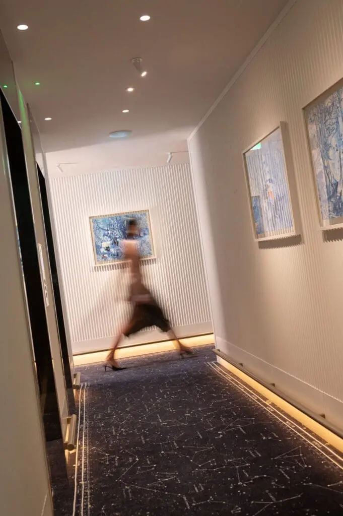 Contemporary hallway at roma art rooms with framed blue artwork on white textured walls and soft lighting.
