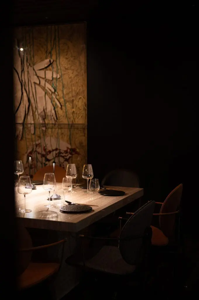 Dining table with several empty wine glasses and black plates, positioned near a wall with abstract artwork at art'otel Rome art hotel.