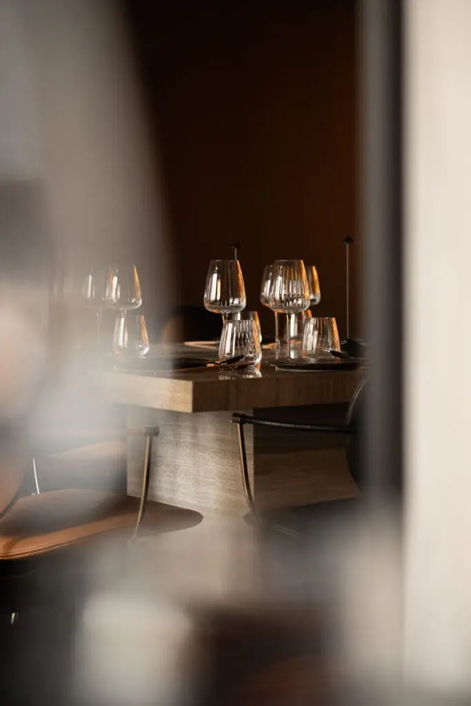 Wooden dining table set with multiple empty wine glasses and plates arranged neatly at art'otel Yezi restaurant Roma.