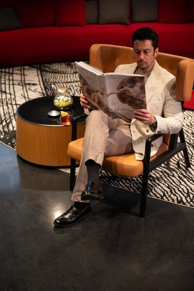 Guest relaxing with an art magazine in a stylish lounge at art gallery art'otel hotel Rome.