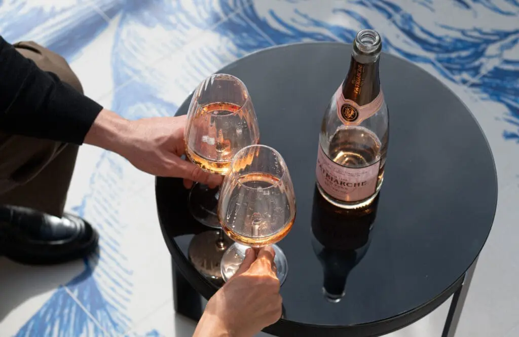 Two hands holding glasses of rosé wine next to a bottle placed on a round black table at rome art rooms.