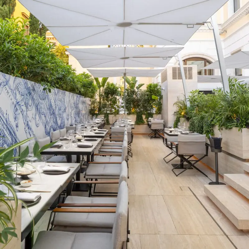 Stylish outdoor dining space at art'otel Luxury art hotel Rome with elegant seating, lush greenery, and artistic wall design.
