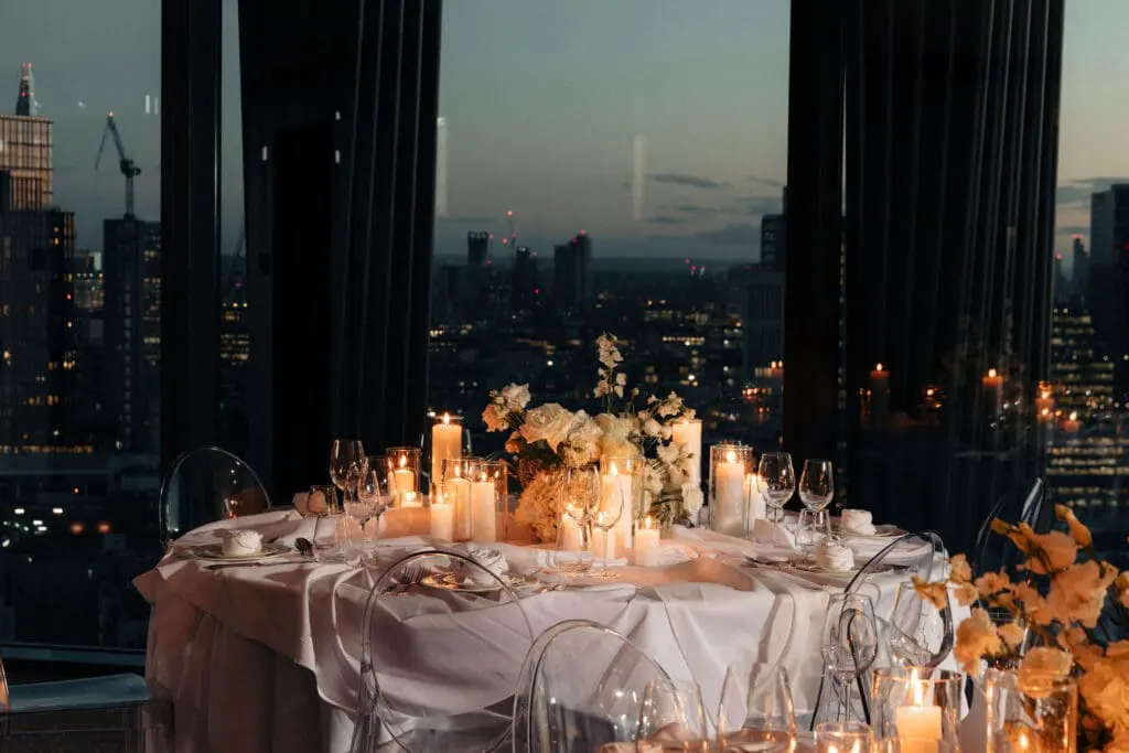 Elegant candlelit dinner table with white flowers and city skyline view at art'otel London Hoxton