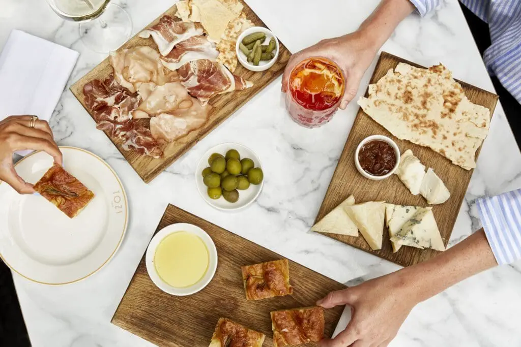 Sharing boards of meats, cheeses, focaccia and olives enjoyed with cocktails, showcasing vibrant dining experiences at art'otel Battersea Power Station restaurant & bar.