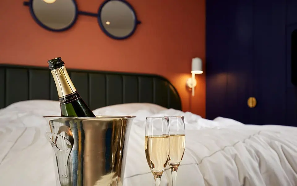 Champagne bottle in ice bucket with two glasses on bed at art’otel Battersea Power Station view room