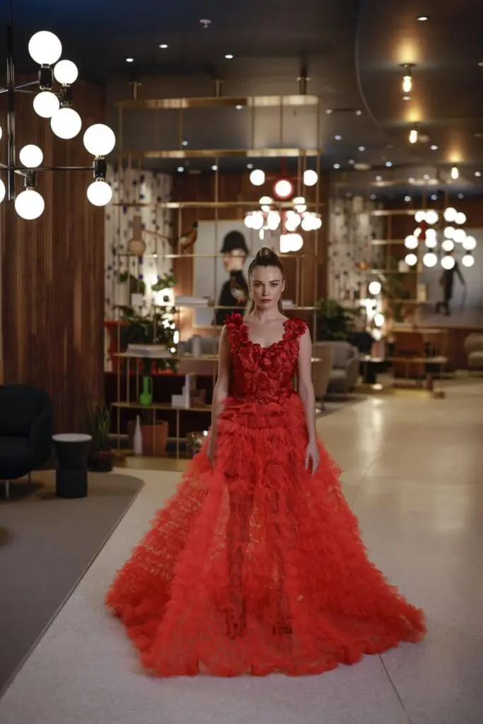 Person wearing an elaborate red gown standing in the stylish art'otel Battersea Power Station lobby with modern lighting and chic decor