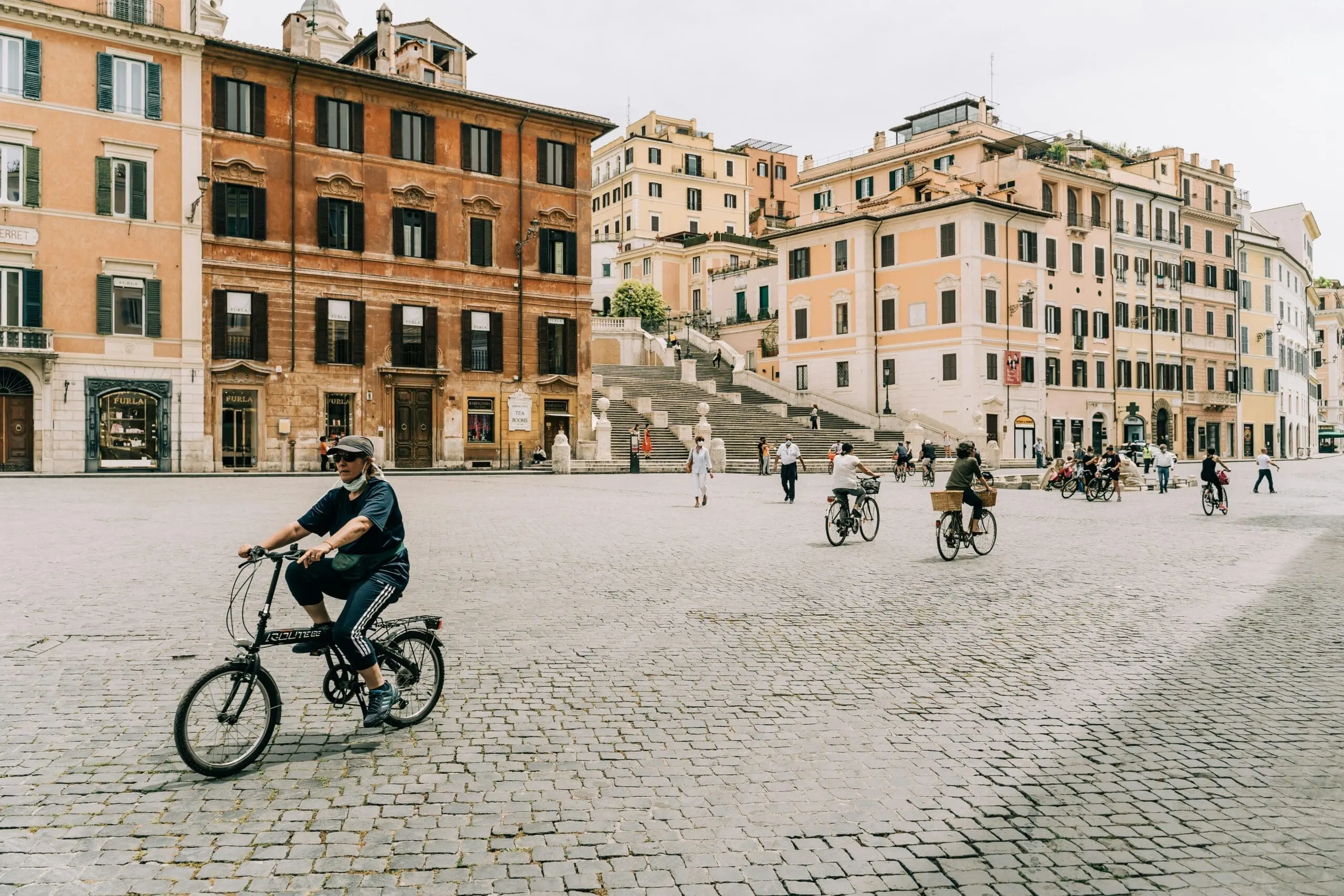 People cycling through historic square near Spanish Steps close to rome art rooms.