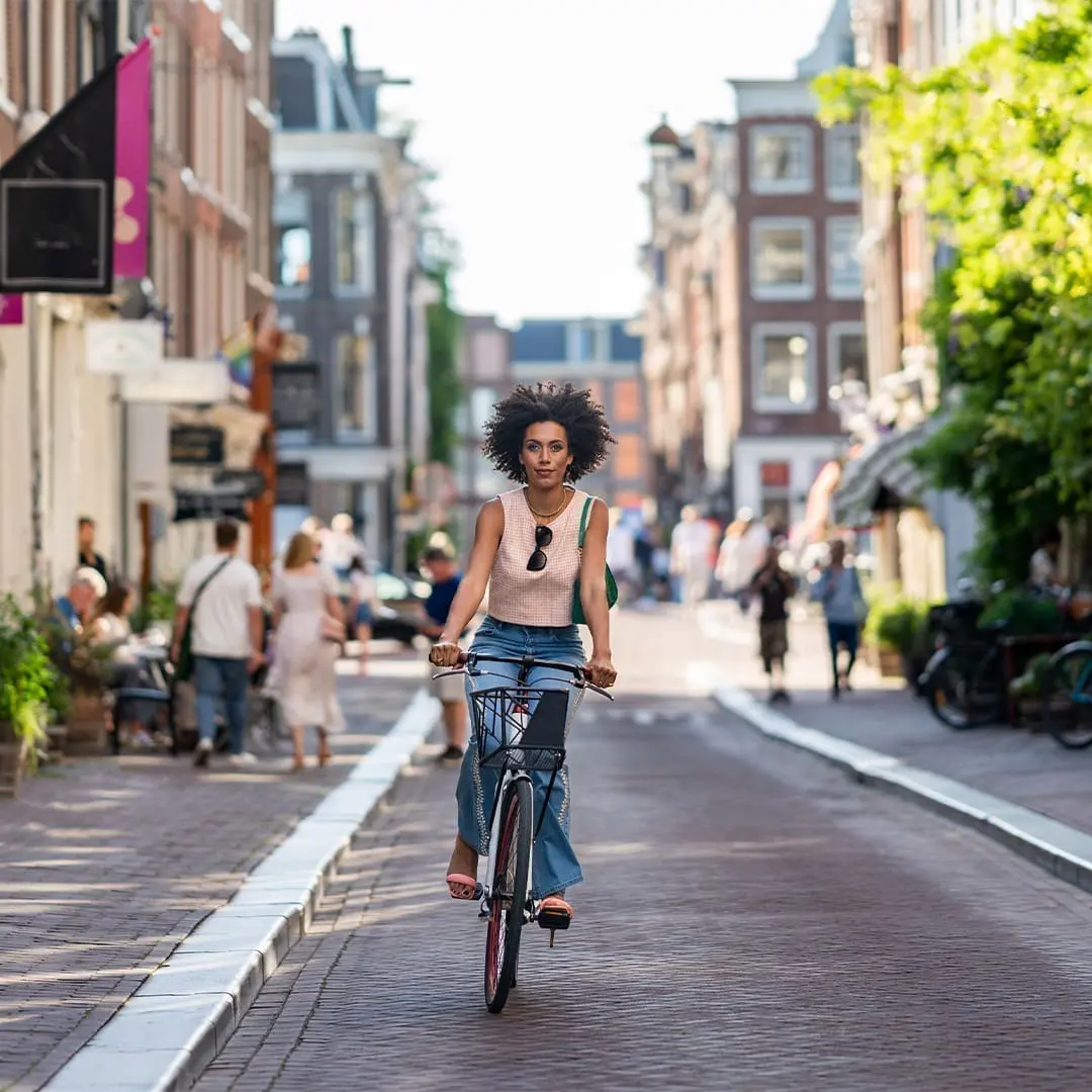 Person cycling through a sunny city street lined with historic buildings and shops, reflecting the vibrant urban lifestyle near art'otel Hotel next to Battersea Power Station.