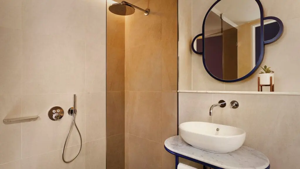 Elegant bathroom at art'otel Battersea Power Station featuring walk-in shower, modern round mirror, stylish sink, and warm lighting.