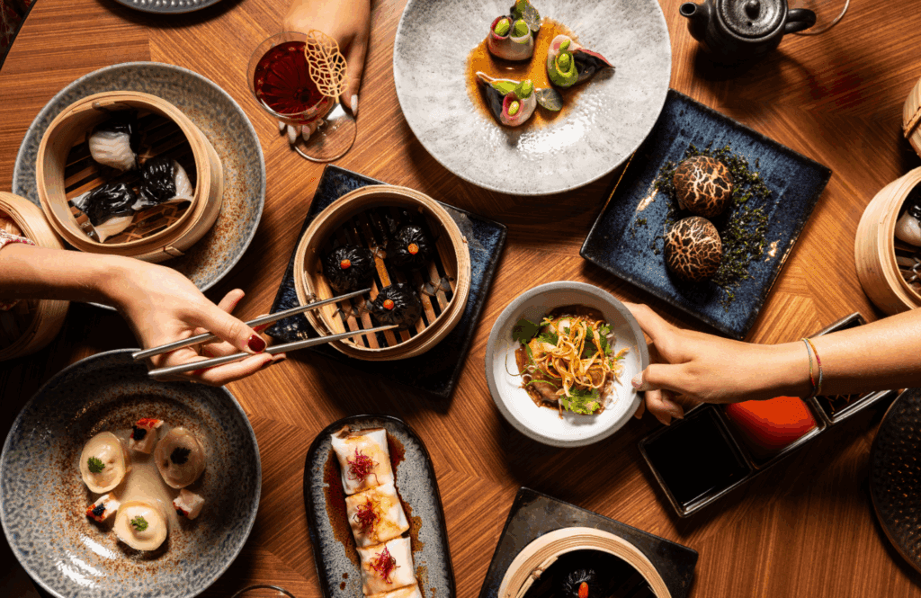 Assorted gourmet dishes at roma art rooms featuring vibrant dim sum, noodles, and elegant plating on a stylish wooden table.