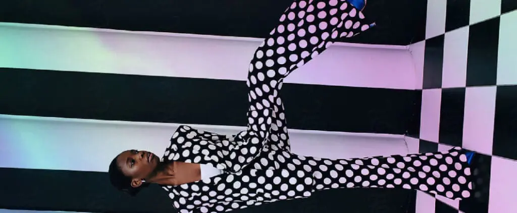 Person wearing bold black-and-white polka dot outfit posing creatively in a modern art installation with striped and checkered walls.