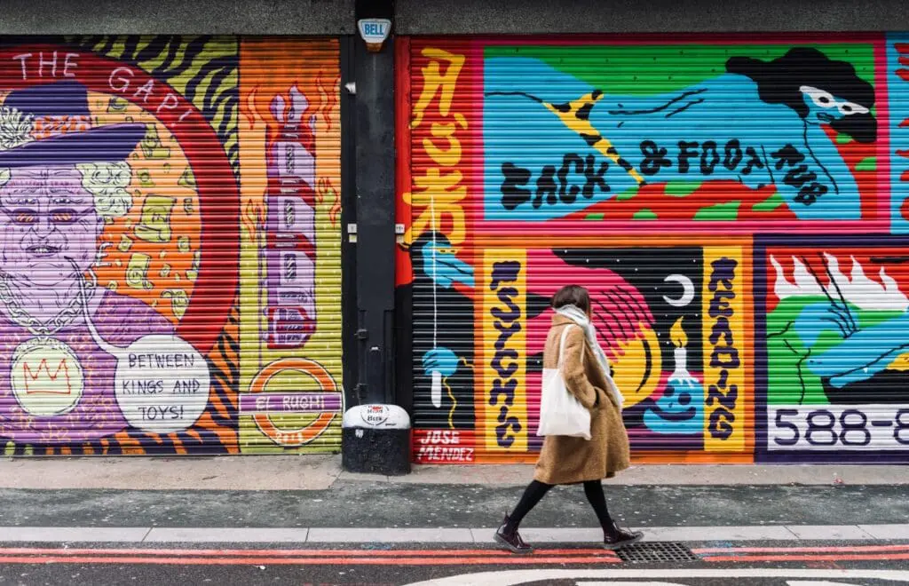 Person walking past colorful street art murals in Shoreditch London near art exhibition