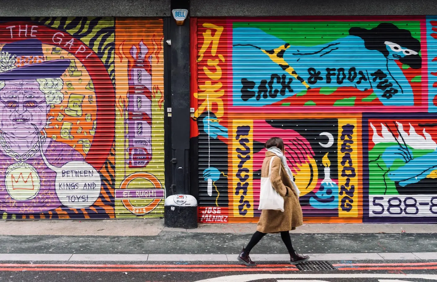 Person walking past colorful street art murals in Shoreditch London near art exhibition