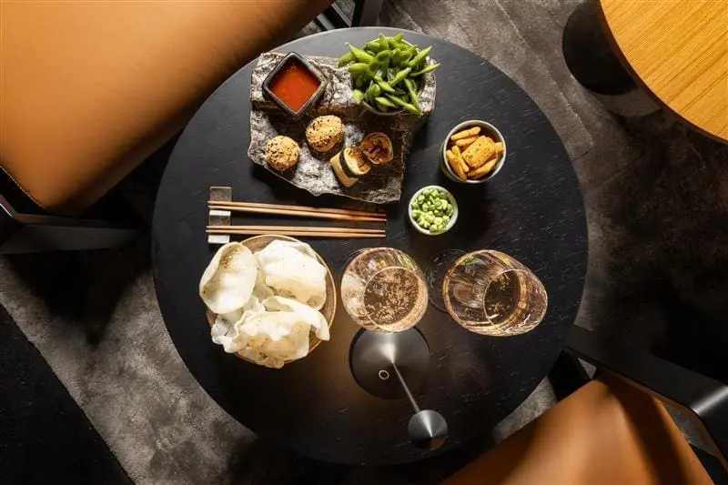 Elegant table setting at rome art rooms featuring Asian appetizers, dipping sauces, edamame, and wine glasses for a refined dining experience.
