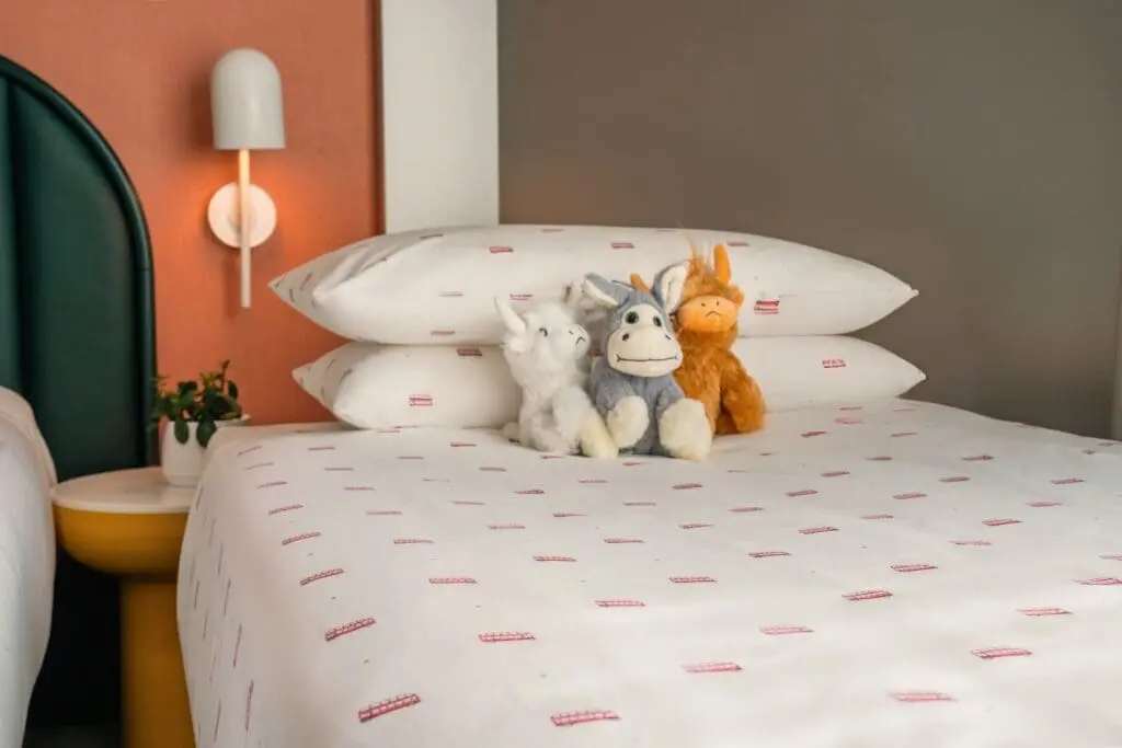 Cozy bed with playful stuffed animals at art'otel Hotel with pool near Battersea Power Station featuring modern design and warm tones.