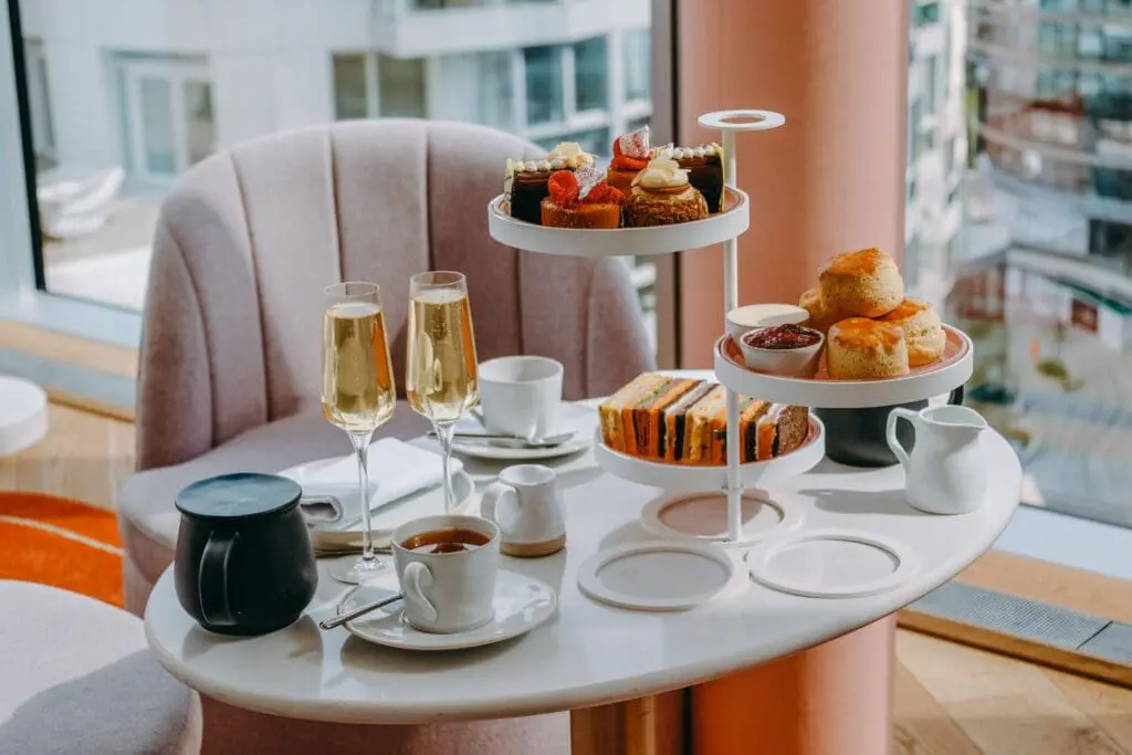 Elegant afternoon tea setup with pastries, scones, sandwiches, and champagne on a white table