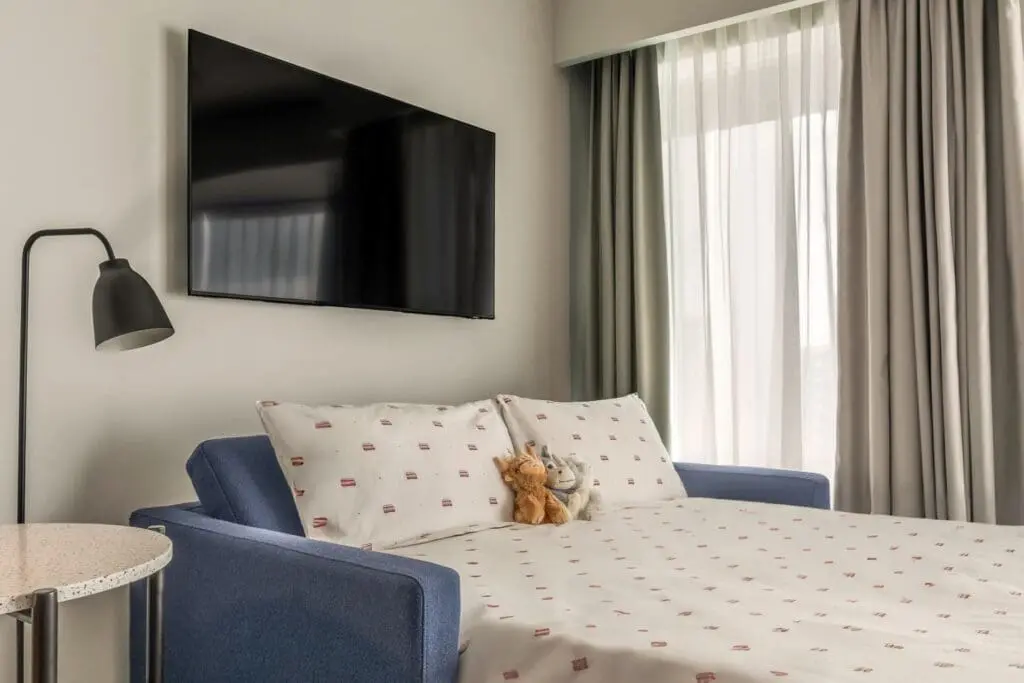 Modern guest room at art'otel Hotel next to Battersea Power Station featuring stylish sofa bed, large TV, and natural light.