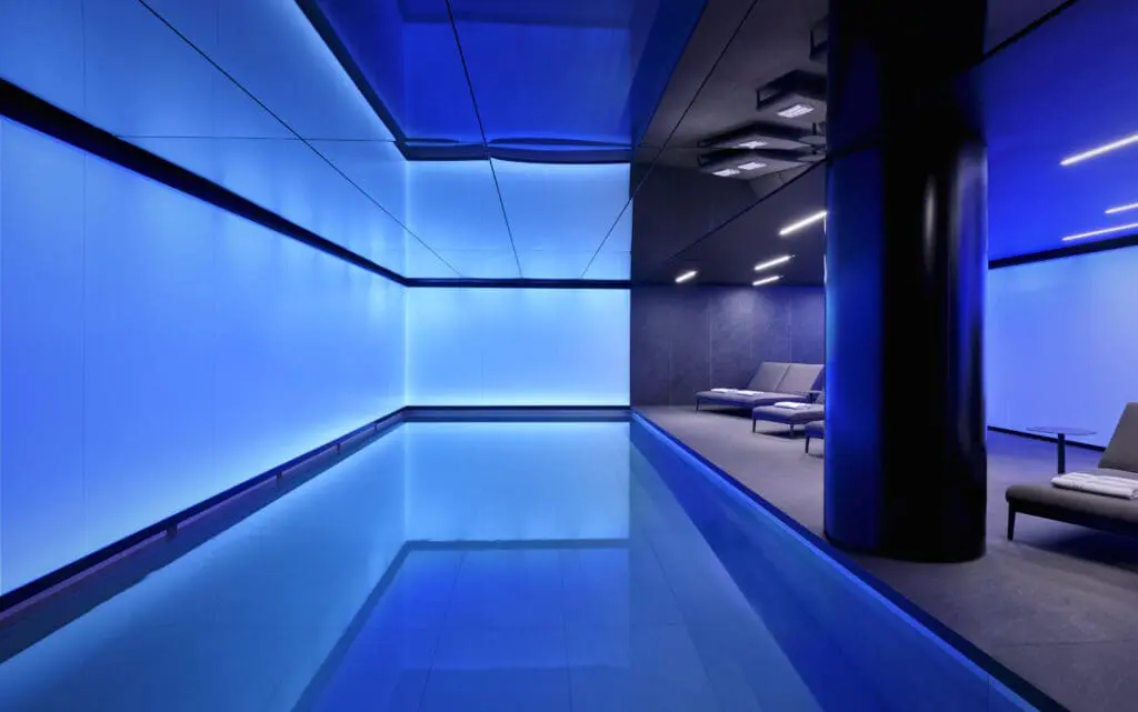 Indoor swimming pool at art'otel London Hoxton Shoreditch hotel with pool, featuring modern blue LED lighting and sleek lounge chairs.