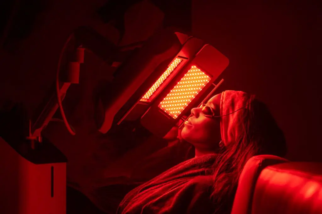 Person receiving advanced LED light therapy treatment in a modern spa room with red illumination and professional skincare equipment.