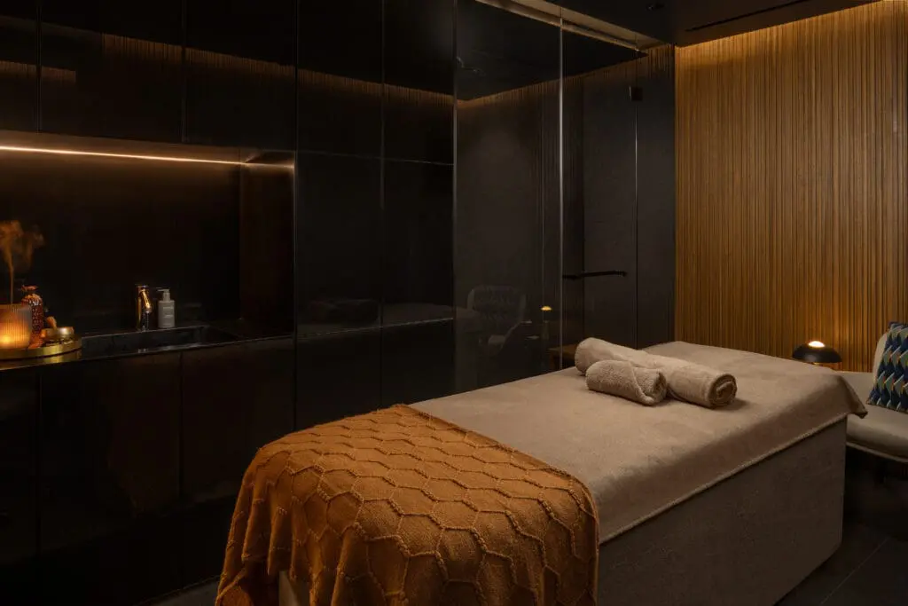 Luxury spa room at art'otel London Hoxton Shoreditch hotel with spa, featuring two massage tables, warm lighting, and elegant wooden accents.