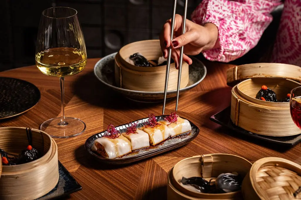 Close-up of gourmet dim sum served on a ceramic plate with wine at art'otel Yezi restaurant Rome, showcasing elegant presentation.