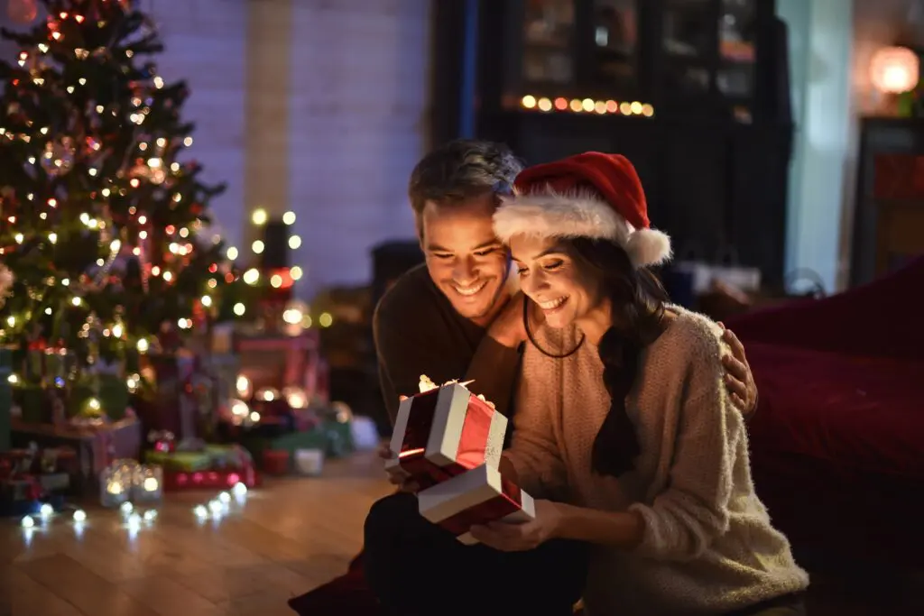 Two people by a Christmas tree opening a gift