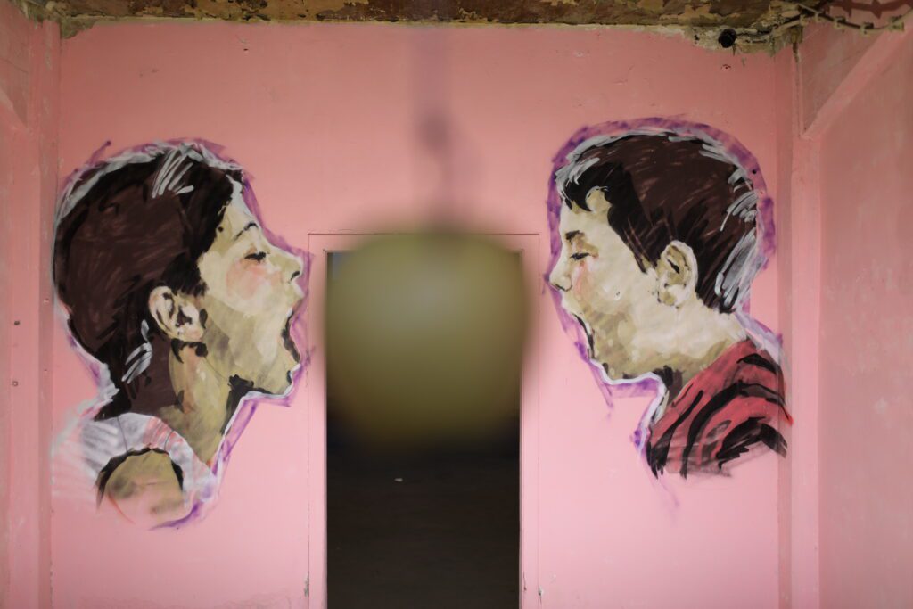 Street art of two children with their mouths open and a real apple hanging from a tree between them.