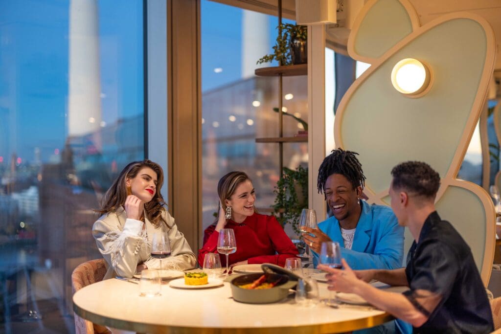 A group of four people sitting at JOIA restaurant, overlooking the Battersea Power Station.