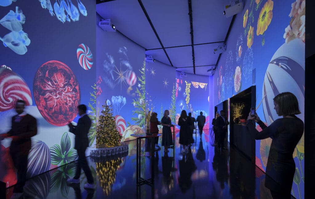People at the gallery at art'otel London Hoxton. The walls are projected with animated Christmas decorations.
