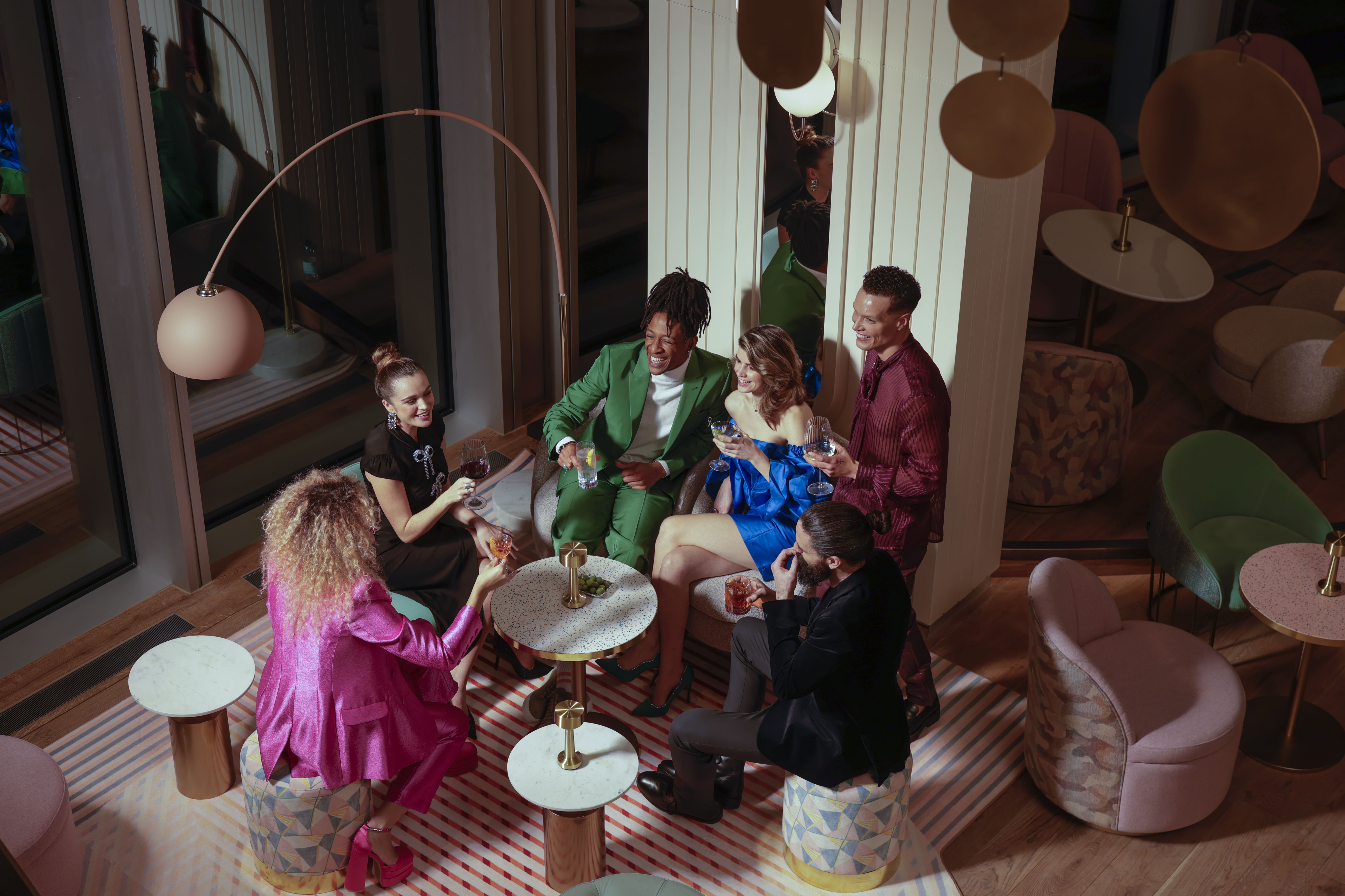 Group enjoying drinks in modern lounge with chic furniture, colorful outfits, stylish decor at art'otel London Hoxton Shoreditch hotel with pool.