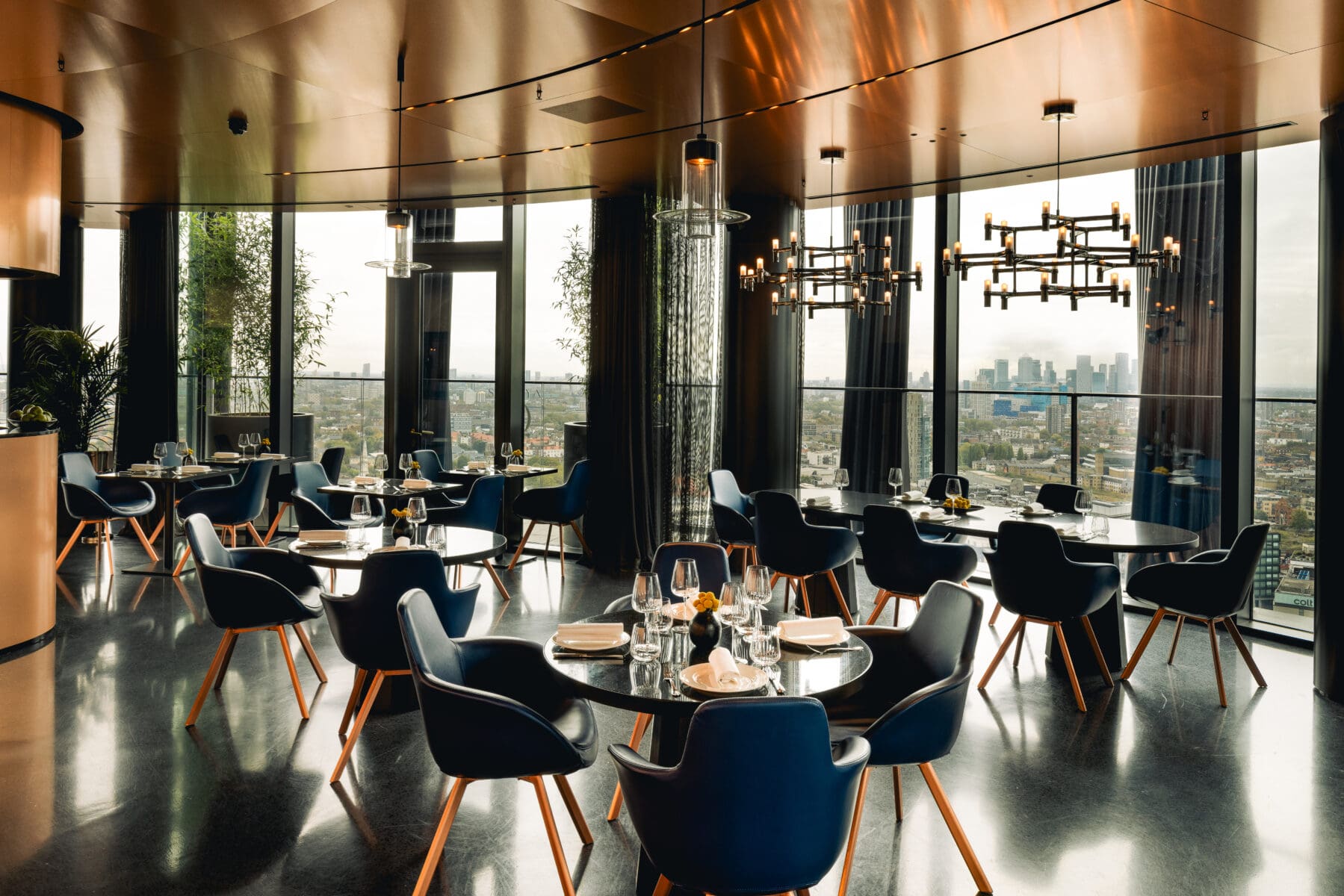 Elegant dining area at art'otel London Hoxton Shoreditch hotel with pool featuring round tables, modern chairs, chic lighting, and panoramic city views.