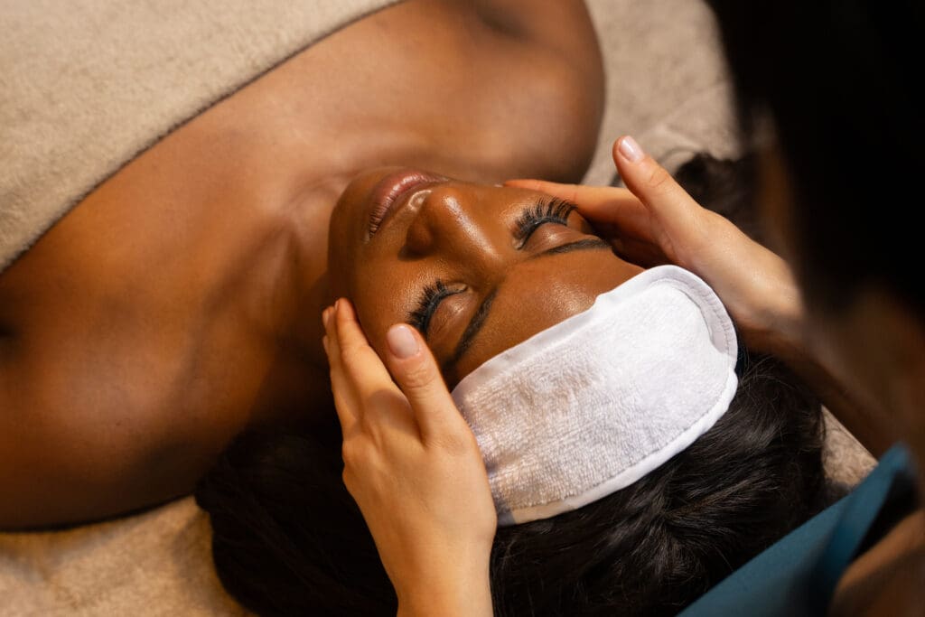 Person lying on a spa bed receiving a gentle facial massage with a white headband in a serene luxury spa setting.
